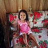 child, girl, smiling, pink_clothing, couch, floral_pattern, indoor, curtains, happy, sitting, barefoot, home, furniture, portrait, cute, young_child, person, casual, daylight, relaxed