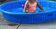 Delilah joined the competition — help win amazing prizes! toddler, child, smiling, water, pool, blue_pool, swimsuit, outdoor, concrete, playful, summer, curly_hair, happy, sitting, daylight, fun, backyard, young_child, plastic_pool, water_play