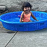 toddler, child, smiling, water, pool, blue_pool, swimsuit, outdoor, concrete, playful, summer, curly_hair, happy, sitting, daylight, fun, backyard, young_child, plastic_pool, water_play