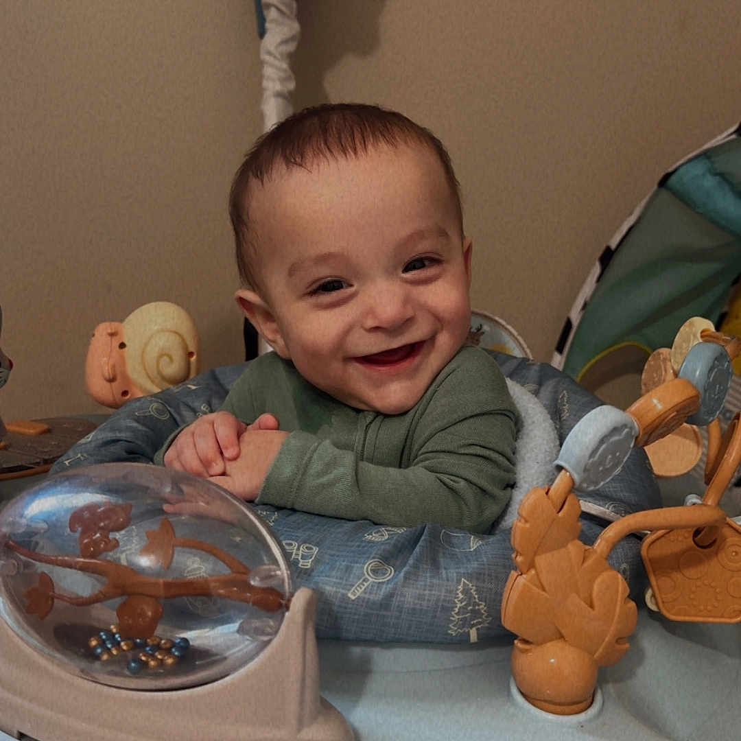 Kayson is registered to the contest to win money with this photo: activity_center, baby, butterfly_toy, carpet, cheerful, child, cute, face, green_clothing, hands, happy, indoor, infant, plastic, play, portrait, seat, smiling, toy, young