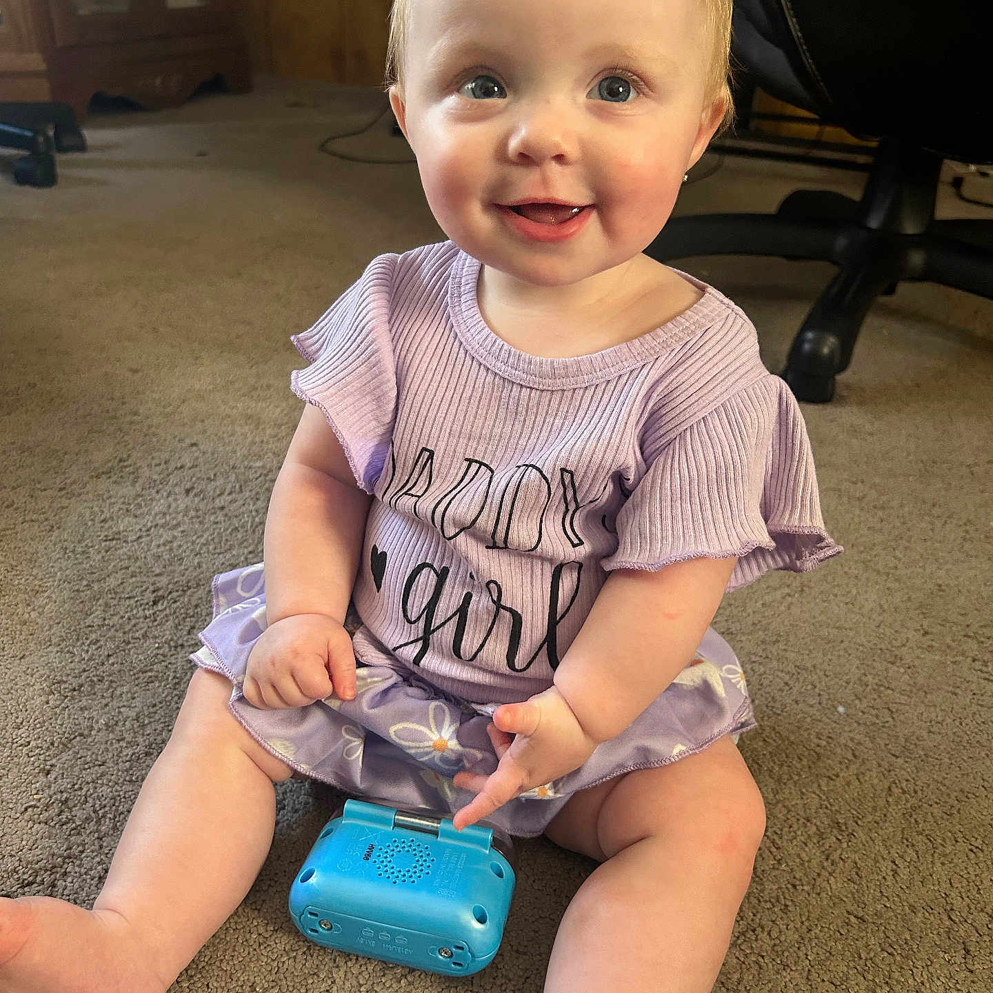 Kennedy is registered to the contest to win money with this photo: baby, bodypart, clothing, couch, diaper, dress, electronics, face, finger, hand, happy, head, mobilephone, person, phone, photography, portrait, sitting, smile, t_shirt