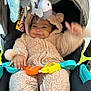 baby, child, stroller, onesie, plush_toys, smiling, happy, infant, cute, soft_toys, playful, wearing_clothes, seated, indoors, colorful, toy_bar, baby_clothing, face, hands, cozy