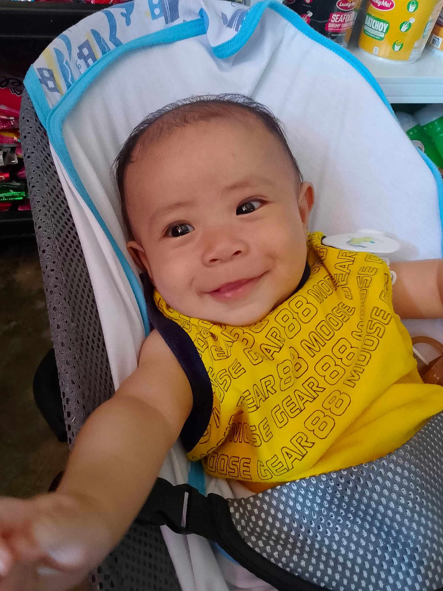 Jeron joined the competition — help win amazing prizes! baby, child, smiling, yellow_bib, seat, indoor, person, happy, infant, reaching, clothing, face, cute, baby_seat, arm, closeup, head, expression, fabric, background