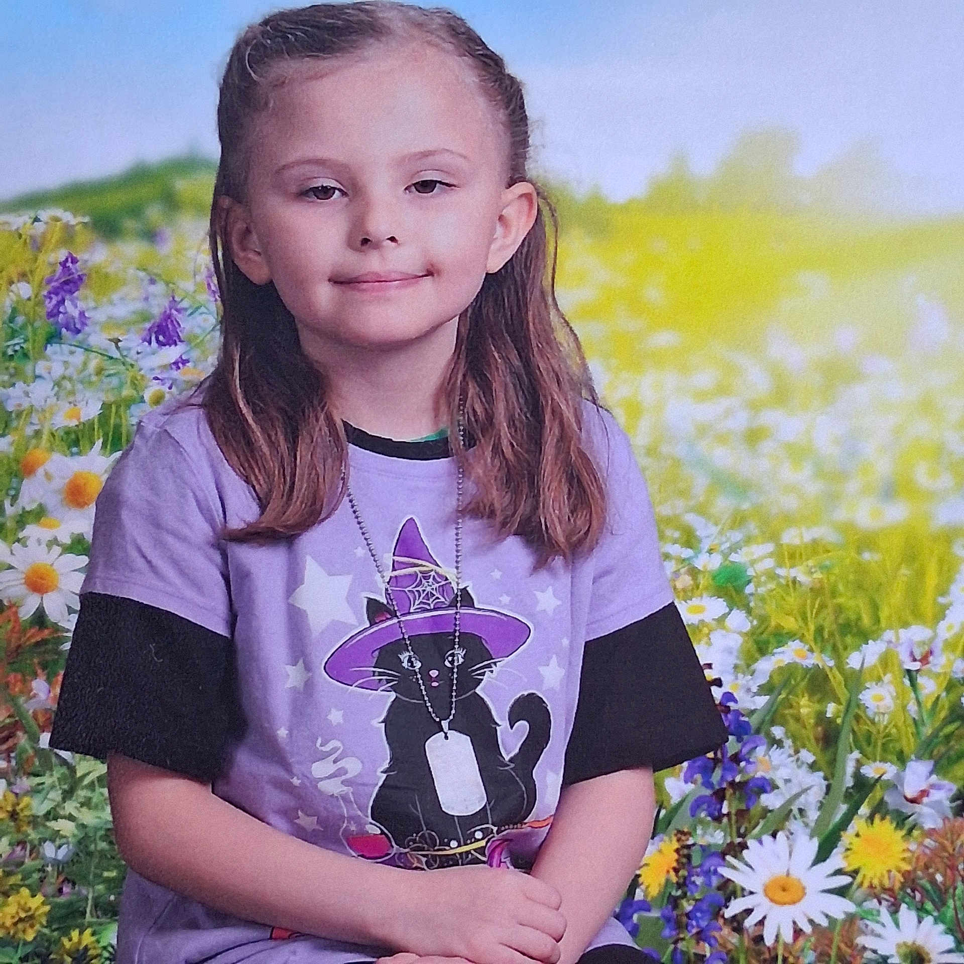 Kara joined the competition — help win amazing prizes! child, girl, smile, purple_shirt, cat_graphic, wildflowers, flowers, nature, outdoor, spring, greenery, portrait, short_hair, sitting, casual_clothing, necklace, colorful, happy, young, scenic
