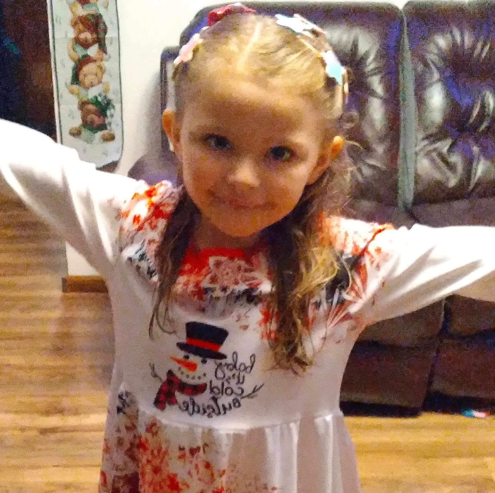 Kara is registered to the contest to win money with this photo: child, girl, smiling, dress, hair_clips, arms_outstretched, indoor, living_room, wooden_floor, couch, holiday_theme, snowman, long_hair, cute, portrait, happy, person, furniture, home, casual