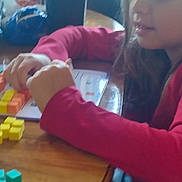 Kara is registered to the contest to win money with this photo: child, girl, red_shirt, wooden_table, blocks, colorful_blocks, markers, indoor, playing, learning, hands, face, long_hair, sitting, casual_clothing, education, toy, focus, activity, home
