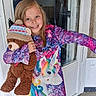 child, girl, teddy_bear, stuffed_animal, unicorn, dress, colorful_clothing, smile, happy, indoors, door, window, long_hair, toy, winter_hat, playful, portrait, person, cute, holding