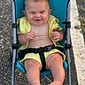 baby, stroller, yellow_clothing, smiling, outdoor, happy, child, legs, feet, seatbelt, blue_stroller, road, casual, summer, infant, skin, person, cute, sitting, portrait
