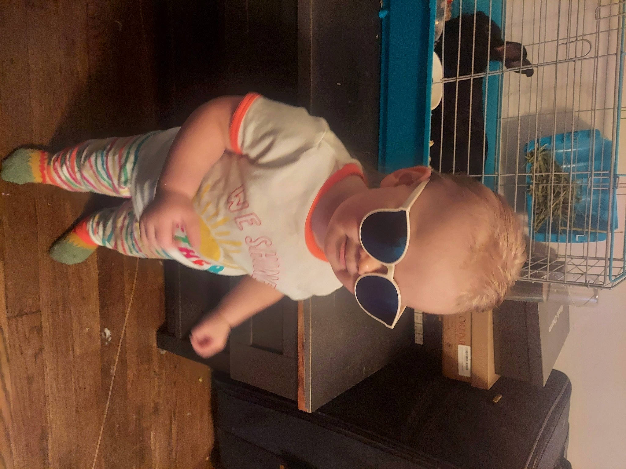 Amy is registered to the contest to win money with this photo: baby, baby_toddler_clothing, child, eyewear, flooring, foot, fun, glasses, hardwood, hat, human_body, human_leg, machine, person, room, sandal, thigh, toddler, toy, visual_arts