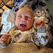 Silas is registered to the contest to win money with this photo: baby, smiling, laughing, blanket, pajamas, animal_print, cozy, infant, happy, cute, child, sleepwear, soft_lighting, indoors, closeup, face, hands, newborn, comfort, resting