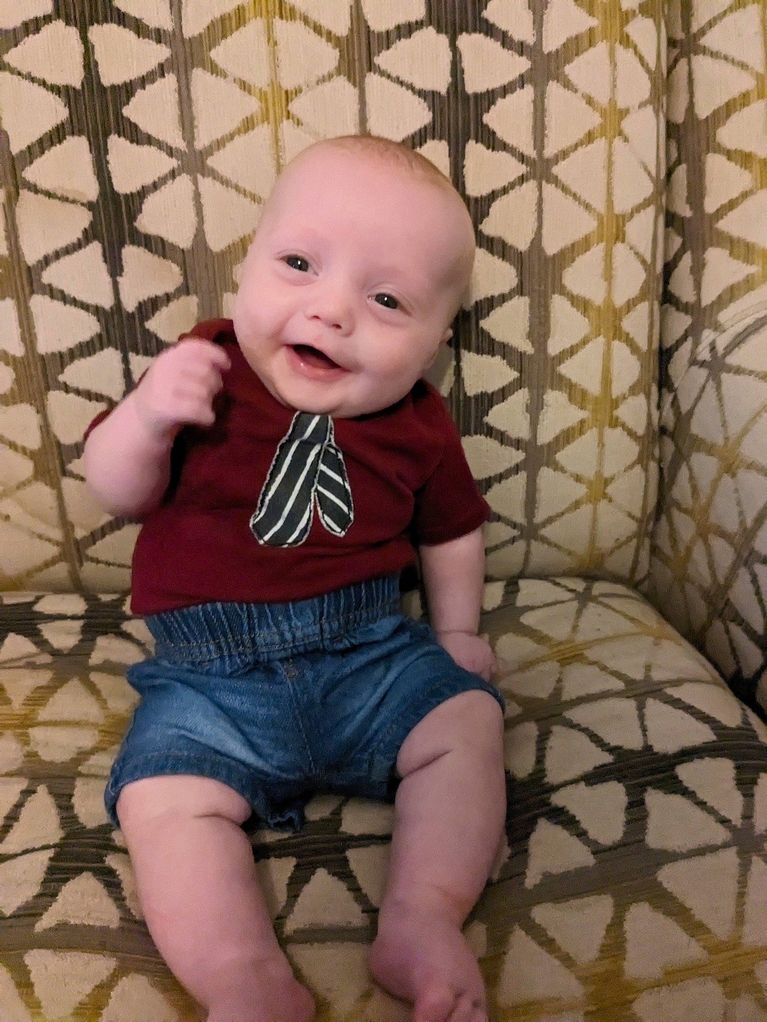 Keenan is registered to the contest to win money with this photo: baby, baby_toddler_clothing, cheek, child, denim, flooring, happy, leg, pattern, person, shirt, shorts, sitting, skin, sleeve, smile, t_shirt, thigh, toddler, waist