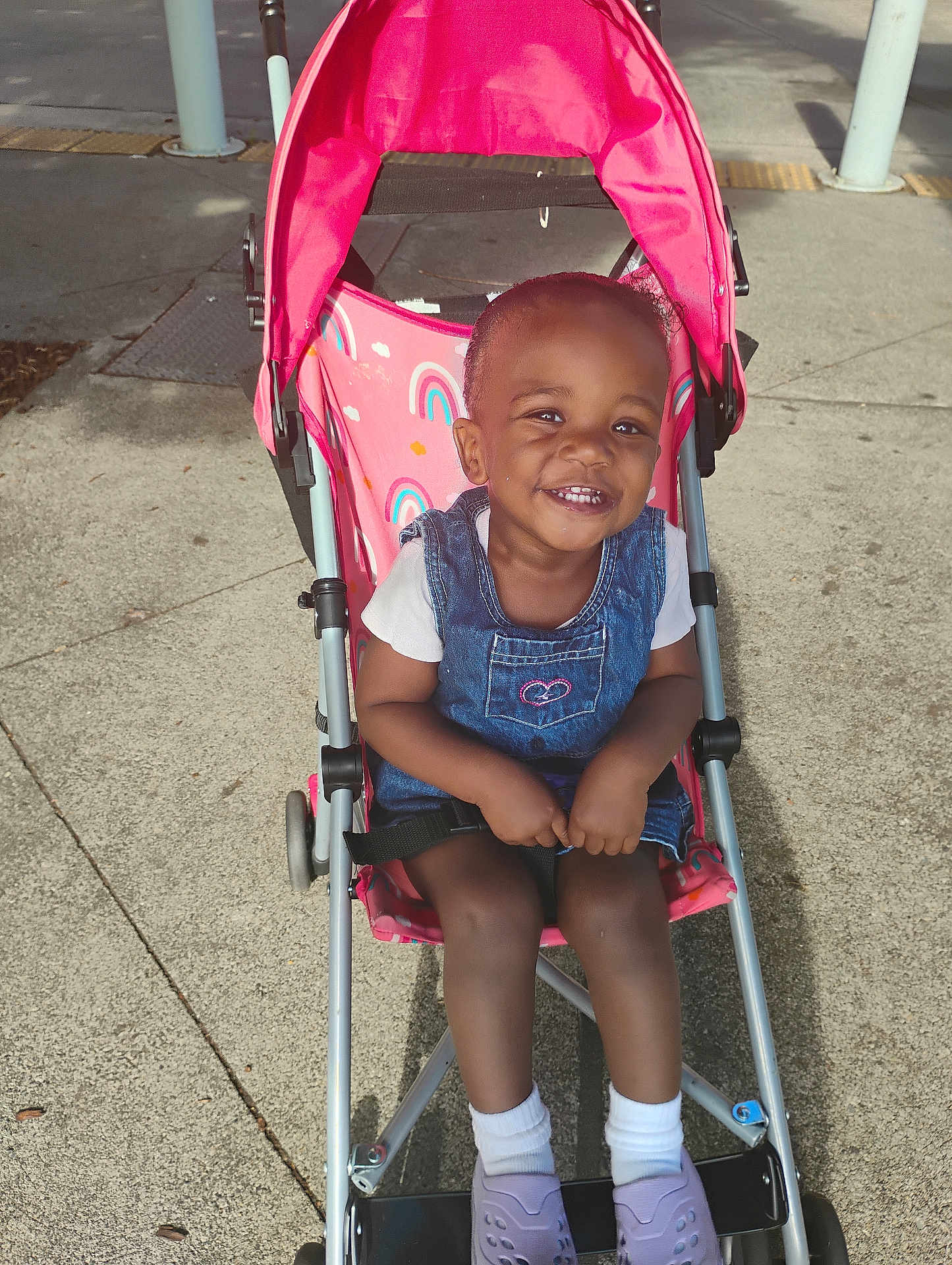 Anyia joined the competition — help win amazing prizes! toddler, child, stroller, pink, rainbow, denim, dress, smile, happy, outdoor, sidewalk, shoes, white_socks, sunlight, concrete, baby, seatbelt, person, cute, daytime