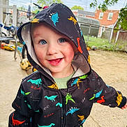 Cru is registered to the contest to win money with this photo: toddler, child, hoodie, dinosaur_pattern, smiling, outdoor, playground, bicycle, ball, joyful, happy, face, clothing, hood, sky, tree, fence, ground, daylight, person