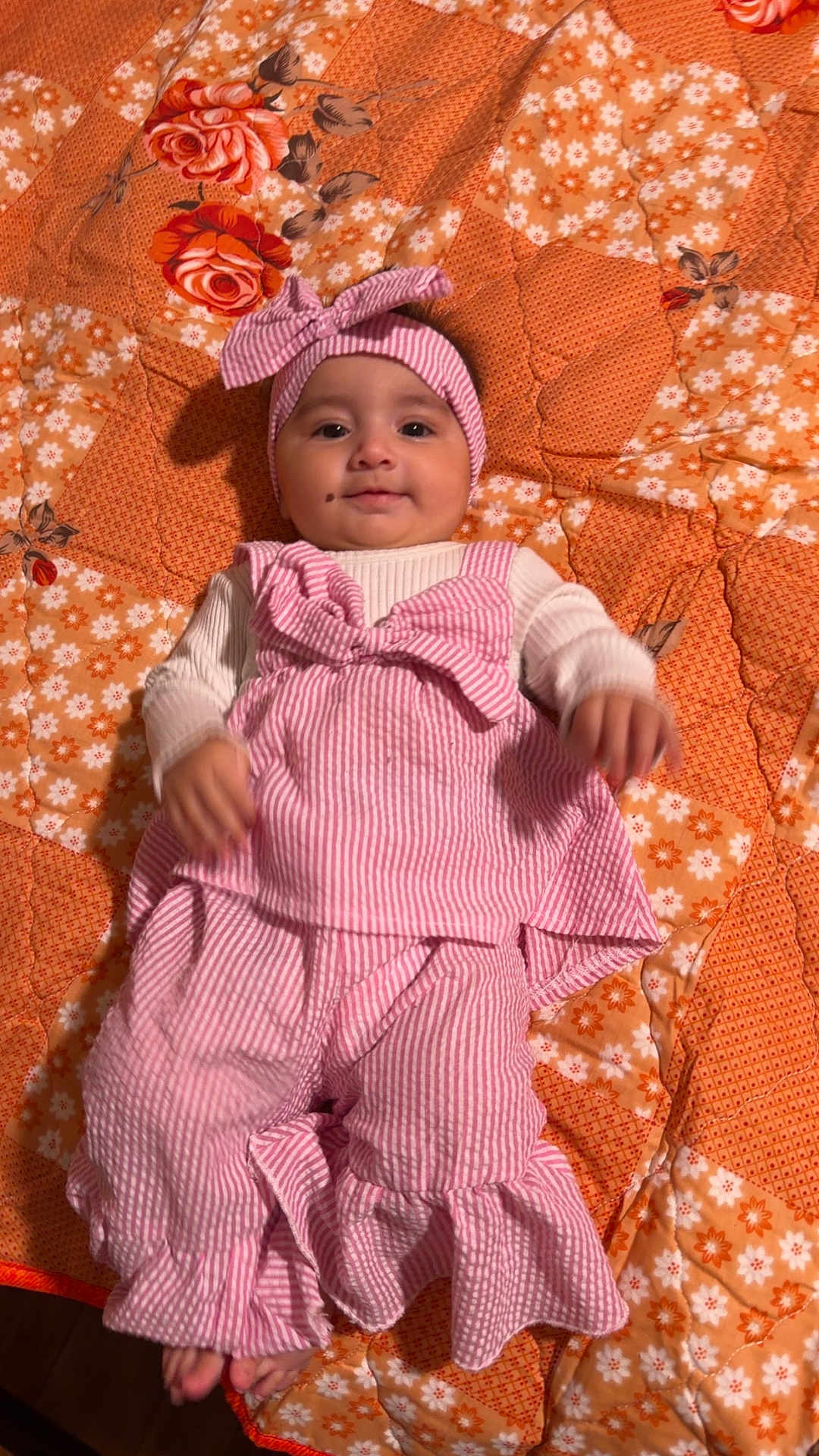 Misl E Zahra joined the competition — help win amazing prizes! baby, infant, child, pink_clothing, headband, striped, quilt, orange, floral_pattern, smiling, lying_down, cute, indoors, portrait, person, small_toes, mole, soft_lighting, fabric, comfortable