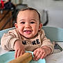 baby, child, smile, happy, high_chair, plate, pastry, food, indoor, table, clothing, face, hands, cute, person, sitting, meal, delicious, breakfast, kitchen