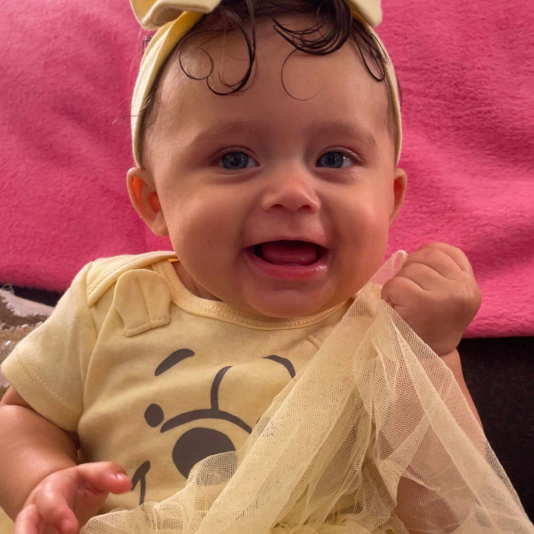 Xiyalize Royalty is registered to the contest to win money with this photo: baby, child, clothing, cute, expression, fabric, face, hands, happy, headband, indoor, infant, person, pink_background, portrait, sitting, smiling, toddler, tulle, yellow_outfit