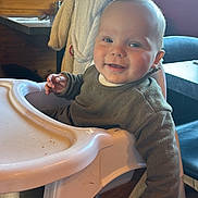 Jonas a rejoint le concours — aidez-le/la à gagner de superbes lots ! baby, high_chair, smiling, indoor, child, wooden_furniture, window, cozy, sweater, table, chair, floor, face, person, light, daylight, happy, infant, cute, restaurant