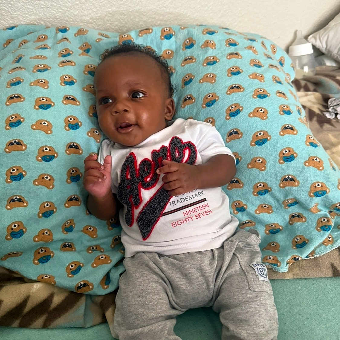 Jasaiah joined the competition — help win amazing prizes! baby, infant, pillow, blue, bear_pattern, mask_pattern, white_shirt, aeropostale, grey_pants, sneakers, jordan_shoes, smiling, cute, indoors, bedroom, blanket, child, young, happy, person