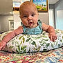 Layla is registered to the contest to win money with this photo: baby, infant, pillow, leaf_pattern, blue_clothing, bedspread, floral, quilt, indoor, wall_art, painting, arm, hand, face, person, bedroom, furniture, curious, closeup, child