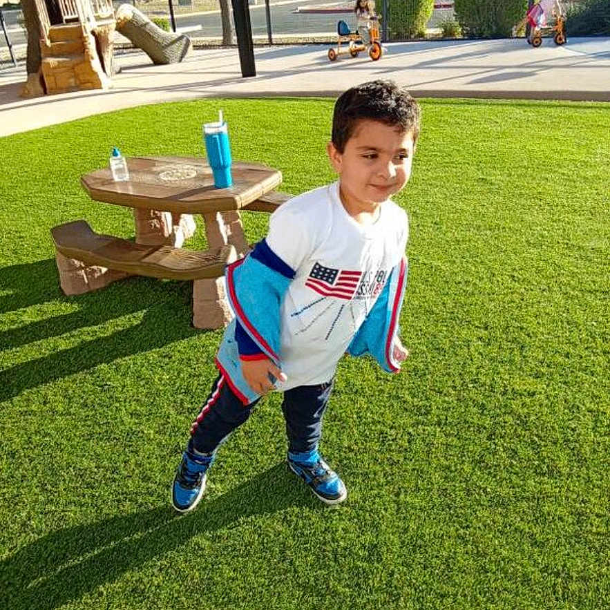 Taha joined the competition — help win amazing prizes! active, blue_shoes, boy, casual_clothing, child, daytime, fence, grass, happy, outdoor, park, picnic_table, play_equipment, playground, recreation, sunlight, trees, tricycle, water_bottle, white_shirt