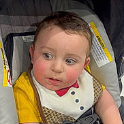 Yusef is registered to the contest to win money with this photo: toddler, child, baby, car_seat, bib, yellow_shirt, rosy_cheeks, seatbelt, indoor, curious, young_child, infant, safety_harness, clothing, person, face, looking_away, cute, car_safety, expression