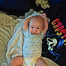 baby, infant, blanket, diaper, blue_onesie, person, face, arms_raised, couch, clothing, graphic_tshirt, ghost_face, home_interior, relaxed, soft_lighting, cute, child, smiling, comfort, casual