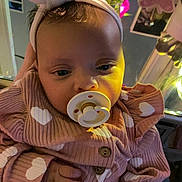 Arielle joined the competition — help win amazing prizes! baby, infant, pacifier, headband, bow, pink_clothing, heart_pattern, onesie, hand, close_up, portrait, indoors, vase, flowers, mirror, reflection, bottle, soft_lighting, sleepy, butterfly_decor