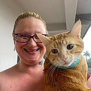 Tiger joined the competition — help win amazing prizes! woman, smiling, glasses, cat, orange_tabby, collar, portrait, indoor, hand, holding, person, happy, face, short_hair, piercing, tattoo, earrings, balcony, window, plant