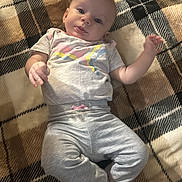Alice is registered to the contest to win money with this photo: baby, infant, blanket, plaid, pattern, floor, wooden_floor, clothing, grey_pants, tshirt, person, child, smiling, cute, lying_down, indoors, skin, head, hand, foot