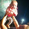 Alice is registered to the contest to win money with this photo: baby, child, fireworks, night, smile, joy, celebration, person, tattoo, arm, clothing, jacket, pants, sandals, outdoor, darkness, light, holding, happy, portrait