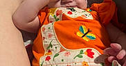 Alice joined the competition — help win amazing prizes! baby, infant, child, orange_clothing, floral_pattern, blanket, plush_toy, legs, feet, hand, face, expression, indoor, person, cute, sleepy, cozy, colorful, fabric, resting