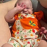 baby, infant, child, orange_clothing, floral_pattern, blanket, plush_toy, legs, feet, hand, face, expression, indoor, person, cute, sleepy, cozy, colorful, fabric, resting