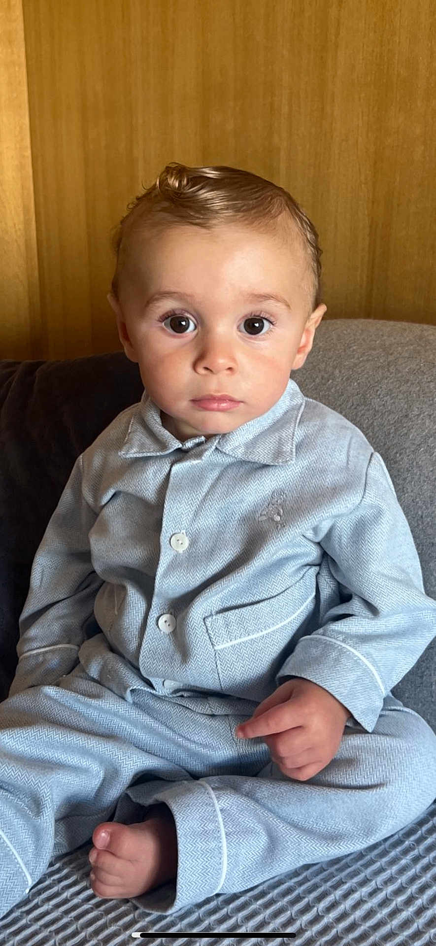 Charles participe au concours pour gagner de l'argent avec cette photo : toddler, child, pajamas, blue_clothing, barefoot, indoor, portrait, curly_hair, big_eyes, seated, blanket, wooden_wall, cute, young_child, face, expression, hands, feet, cozy, soft_lighting