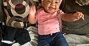Aliza joined the competition — help win amazing prizes! baby, child, smiling, pink_headband, pink_shirt, jeans, white_socks, couch, pillow, blanket, happy, indoors, infant, person, sitting, cute, home, cozy, patterned_pillow, waving