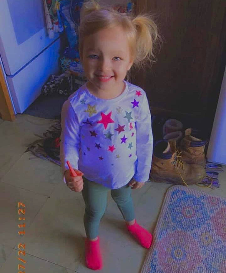 Ellie is registered to the contest to win money with this photo: arm, baby_toddler_clothing, blond, blue, child, curtain, electric_blue, floor, flooring, happy, human_body, human_leg, joy, knee, person, pink, purple, sleeve, smile, t_shirt