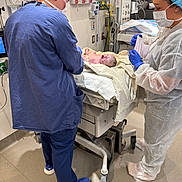 Irene joined the competition — help win amazing prizes! newborn, baby, hospital, medical_staff, scrubs, mask, gloves, medical_equipment, crib, infant, healthcare, clinic, delivery_room, person, face, protective_gear, blue_shoes, white_floor, towel, hospital_gown