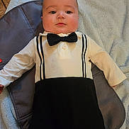 Toby joined the competition — help win amazing prizes! baby, infant, child, bow_tie, onesie, blanket, clothing, face, chubby_cheeks, lying_down, portrait, eyes, hand, outfit, tile_floor, soft_texture, fabric, neutral_expression, gaze, indoor