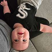 Toby is registered to the contest to win money with this photo: baby, infant, child, upside_down, black_shirt, grey_pants, couch, textured_fabric, smiling, happy, face, eyes, head, person, indoors, casual_clothing, relaxed, cute, skin, baby_clothes
