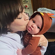 Toby is registered to the contest to win money with this photo: affection, baby, bookshelf, brown_clothing, child, cozy, face, family, hooded_outfit, hug, indoor, intimate, kiss, love, person, portrait, sitting, warmth, woman, wooden_wall