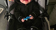 Toby is registered to the contest to win money with this photo: baby, black_fleece, blue_toy, bright_eyes, car_seat, carseat_handle, chubby_cheeks, floor_carpet, gray_textile, happy, hooded_outfit, indoors, infant, plush_slippers, portrait, seat_padding, seat_strap, smiling, toy_in_hand, warning_label