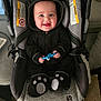 Toby is registered to the contest to win money with this photo: baby, infant, smiling, car_seat, hooded_outfit, black_fleece, plush_slippers, blue_toy, seat_strap, warning_label, seat_padding, chubby_cheeks, bright_eyes, portrait, indoors, carseat_handle, gray_textile, happy, toy_in_hand, floor_carpet
