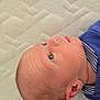 baby, newborn, infant, face, head, blue_clothing, ribbed_fabric, striped_collar, skin, ear, eye, nose, mouth, lying_down, textured_surface, mattress, portrait, close_up, child, curious