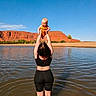 baby, woman, water, lake, outdoor, sky, red_rocks, cliffs, nature, child, holding, playful, sunlight, summer, recreation, happy, person, back_view, parent, lifting