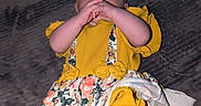 Juniper is registered to the contest to win money with this photo: baby, baby_girl, child, closeup, curious_expression, cute, floral_pattern, hands_near_mouth, headband, headwear, indoor, infant, infant_clothing, legs, lying_down, person, portrait, skin, soft_surface, yellow_clothing