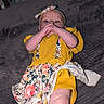 Juniper is registered to the contest to win money with this photo: baby, baby_girl, child, closeup, curious_expression, cute, floral_pattern, hands_near_mouth, headband, headwear, indoor, infant, infant_clothing, legs, lying_down, person, portrait, skin, soft_surface, yellow_clothing