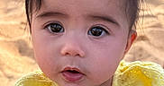 Persephone is registered to the contest to win money with this photo: baby, child, infant, portrait, close_up, face, eyes, brown_hair, yellow_clothing, outdoor, beach, sand, sunlight, windblown_hair, wide_eyed, open_mouth, sitting, photography, adorable, toddler