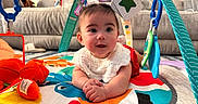 Persephone joined the competition — help win amazing prizes! baby, child, infant, tummy_time, smiling, sitting, playmat, play_gym, toys, colorful, indoors, living_room, couch, portrait, face, hands, bib, baby_clothing, soft_toys, happy