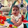 baby, child, infant, sitting, play_mat, baby_gym, toys, plush_toy, colorful, indoors, living_room, couch, portrait, face, eyes, open_mouth, smiling, hands, bib, playtime