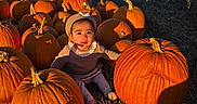 Persephone is registered to the contest to win money with this photo: baby, child, pumpkin, pumpkin_patch, farm, outdoor, autumn, fall, harvest, halloween, portrait, sitting, hat, sweater, smiling, sunlight, golden_hour, mountains, clouds, fence