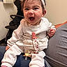 baby, child, infant, smiling, laughing, portrait, headband, bow, white_outfit, pink_socks, pacifier, seated, lap, indoor, home, office_chair, couch, adult_lap, happy, photography